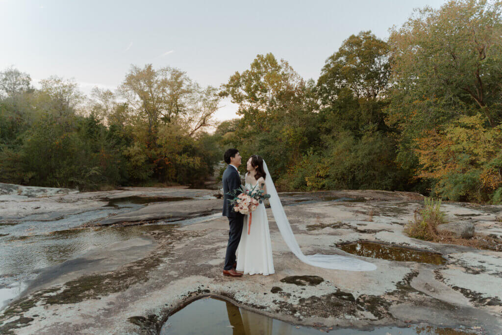 A couple smiling on the rocks alongside the creek, in Autumn