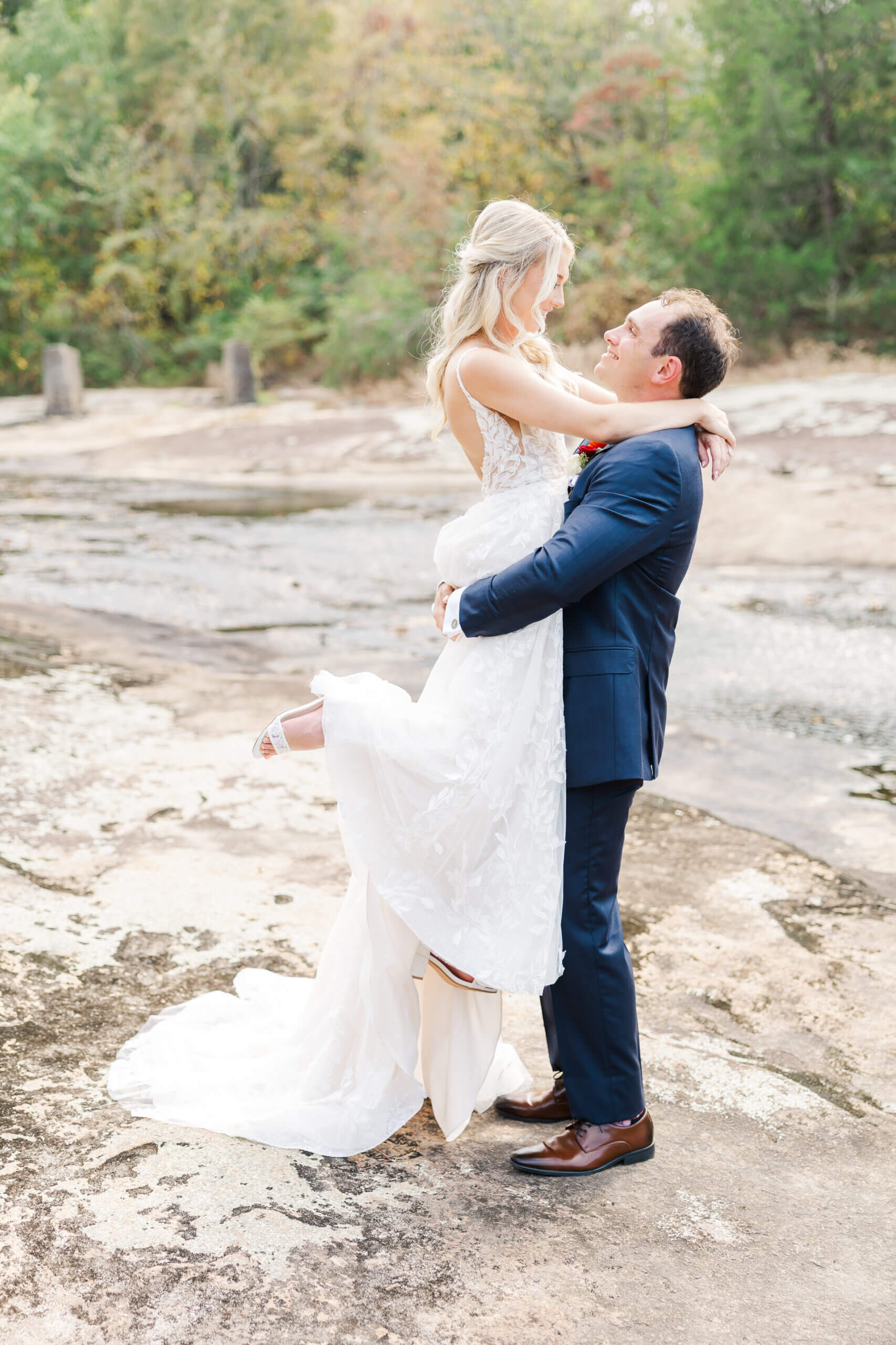 Couple by the creek groom lifting up bride for romantic photo.